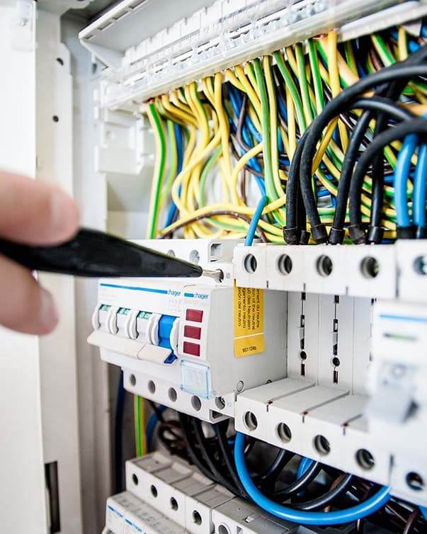 Werk in een geopende groepenkast: met een schroevendraaier wordt een aansluiting op de rij automaten vastgezet, met daarboven de blauwe, zwarte en geelgroene aders.