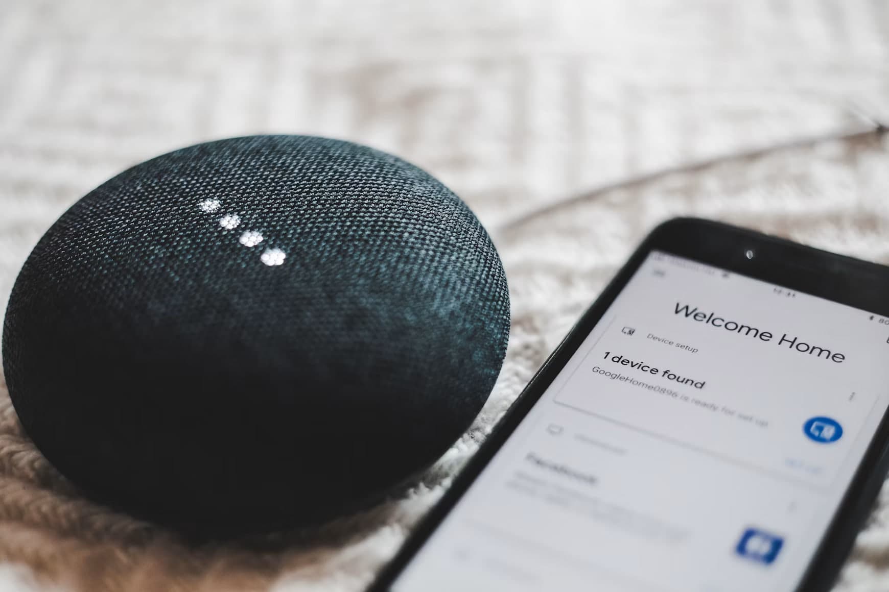 Een slimme speaker op een gebreide plaid, met daarnaast een telefoon waarop de app een nieuw apparaat heeft gevonden om in te stellen.