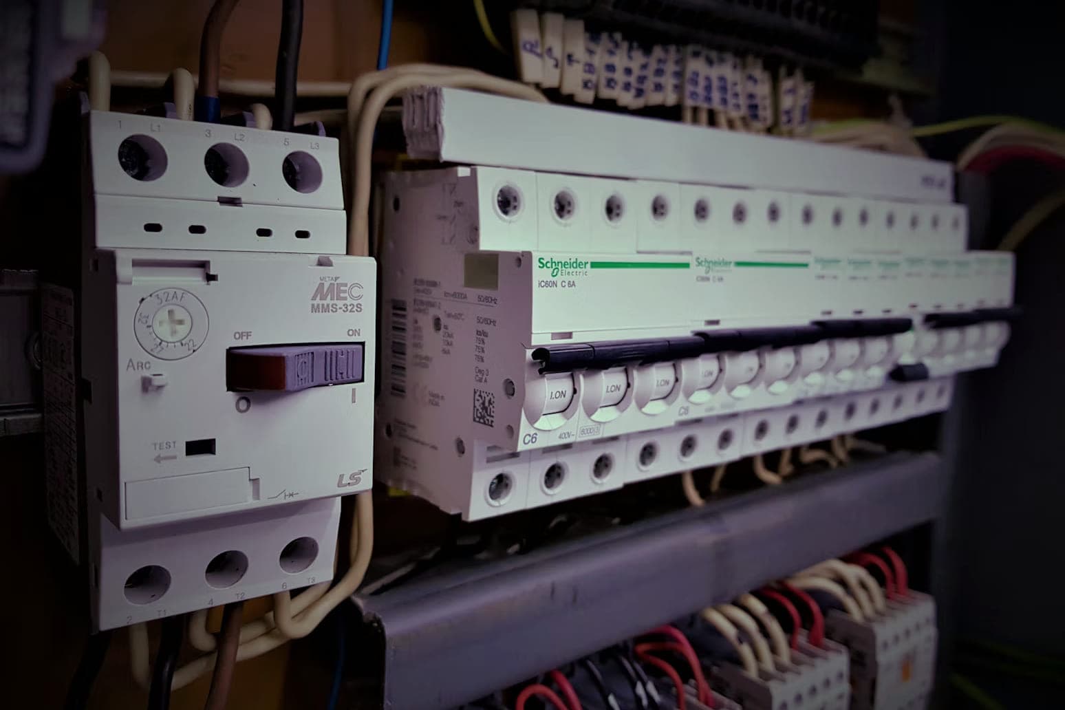 Een rij automaten naast een motorbeveiligingsschakelaar op de DIN-rail van een verdeelkast, met de aders eronder op klemmenrijen.