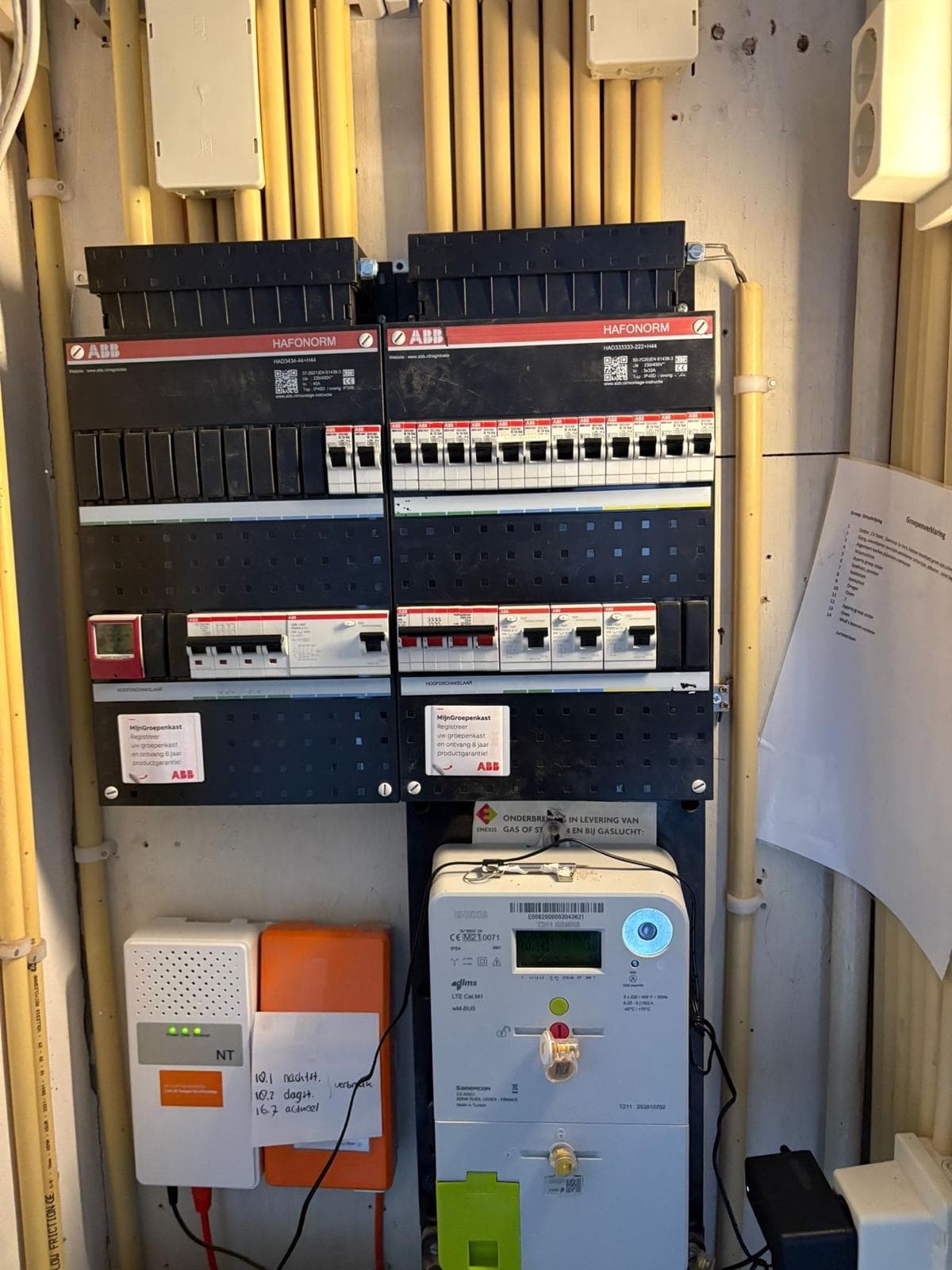 Twee ABB-verdeelkasten naast elkaar in een meterkast: rijen automaten en aardlekschakelaars, de slimme meter eronder en de installatiebuizen die in strakke rijen langs de wand omhoog lopen.