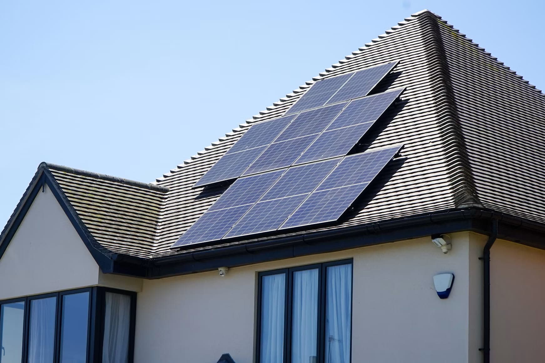 Zonnepanelen op het pannendak van een woning, getrapt gelegd langs de schuine dakrand, tegen een blauwe lucht.